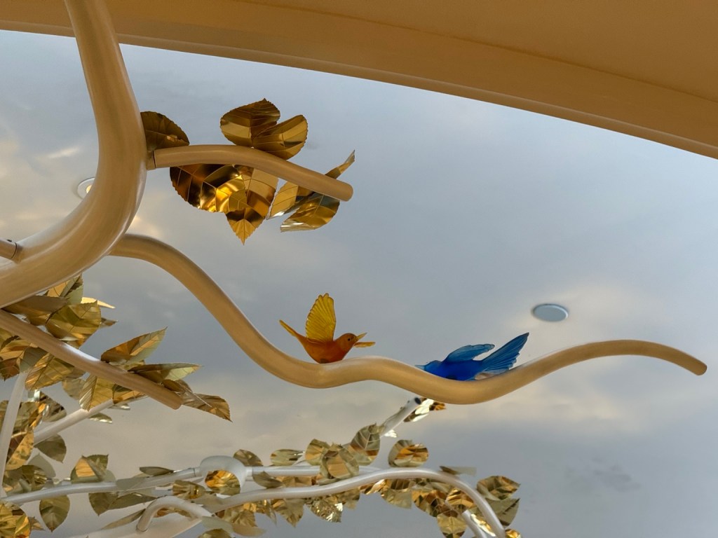Small blue birds perched among glistening gold flowers on the branches of a decorative tree at The Venetian.
