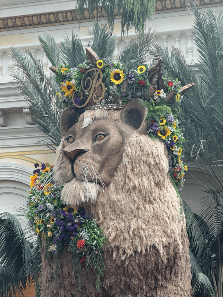 Lion sculpture with a textured mane and a crown decorated with sunflowers and other colorful flowers at the Bellagio Conservatory.

