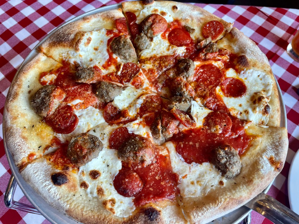 Pizza topped with pepperoni and meatballs on a metal tray over a red-and-white checked tablecloth at Grimaldi’s Pizzeria.